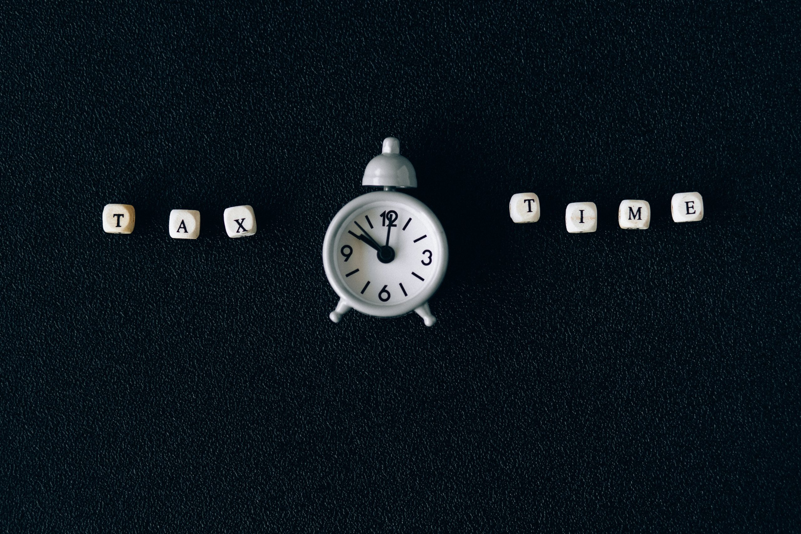 white clock placed on a black background with the letter tax time beside it